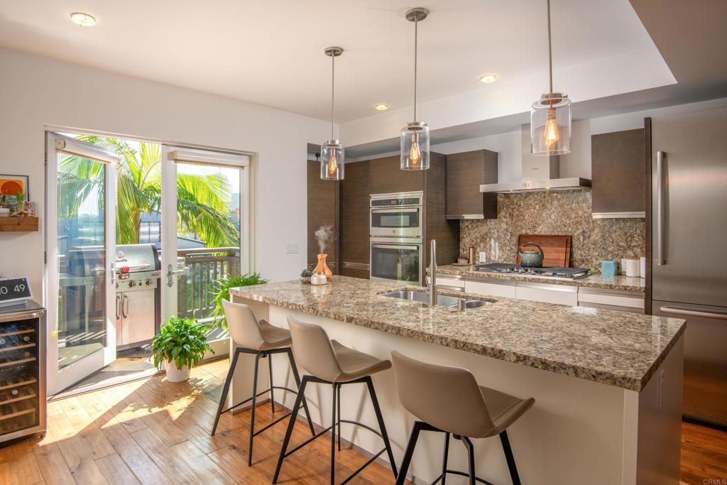 90 North Coast Highway 101, Unit 310 Encinitas, CA 92024 - Photo 4 of 24 a kitchen with kitchen island granite countertop a stove a refrigerator a oven a sink with a dining table and chairs with wooden floor