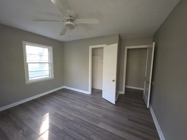 an empty room with wooden floor ceiling fan and windows