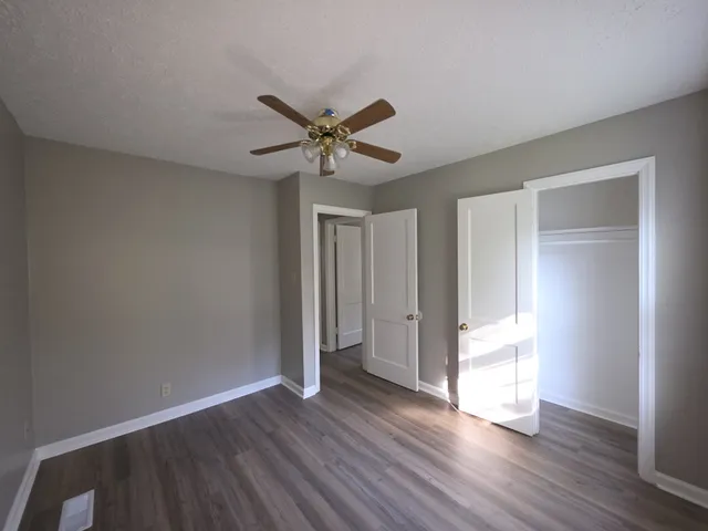 a view of an empty room with wooden floor and a ceiling fan