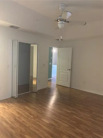 a view of an empty room with wooden floor ceiling fan