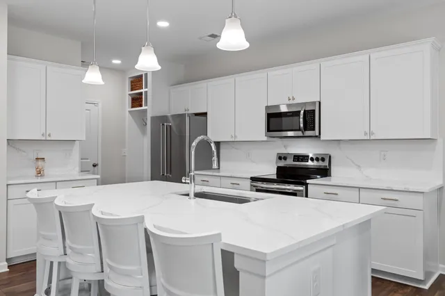 a kitchen with stainless steel appliances a sink a stove a refrigerator cabinets and chairs