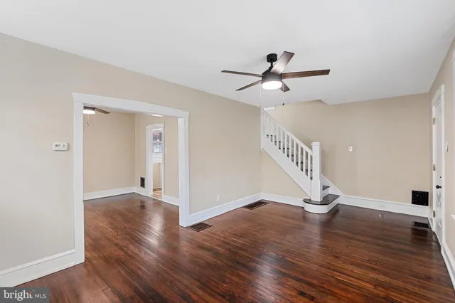 a view of an empty room with wooden floor and a ceiling fan