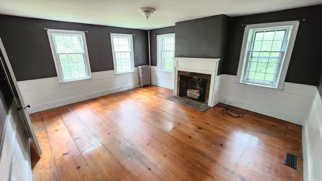 an empty room with wooden floor fireplace and windows