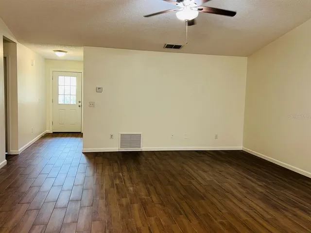 an empty room with wooden floor chandelier fan and windows