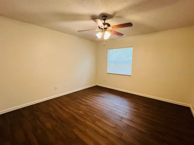 a view of an empty room with wooden floor and a fan