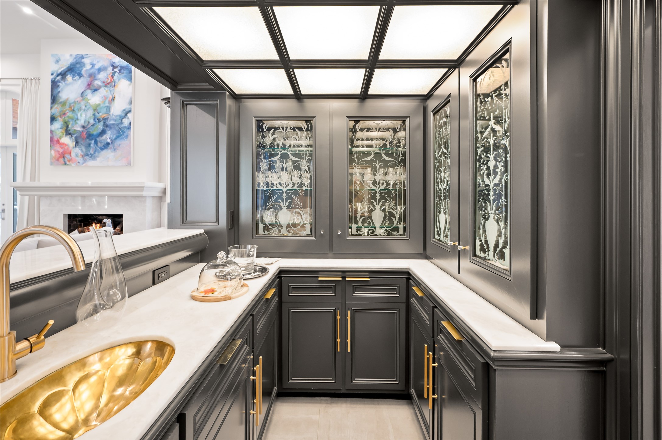 11518 Shadow Way Street Houston, TX 77024 - Photo 9 of 50 The Wet Bar, situated just off the Great Room/ Formal Living Room, features rich charcoal cabinetry, brass hardware, etched glass-front doors, and a marble countertop with a stunning gold sink. This glamorous space is ideal for serving cocktails or displaying curated glassware.