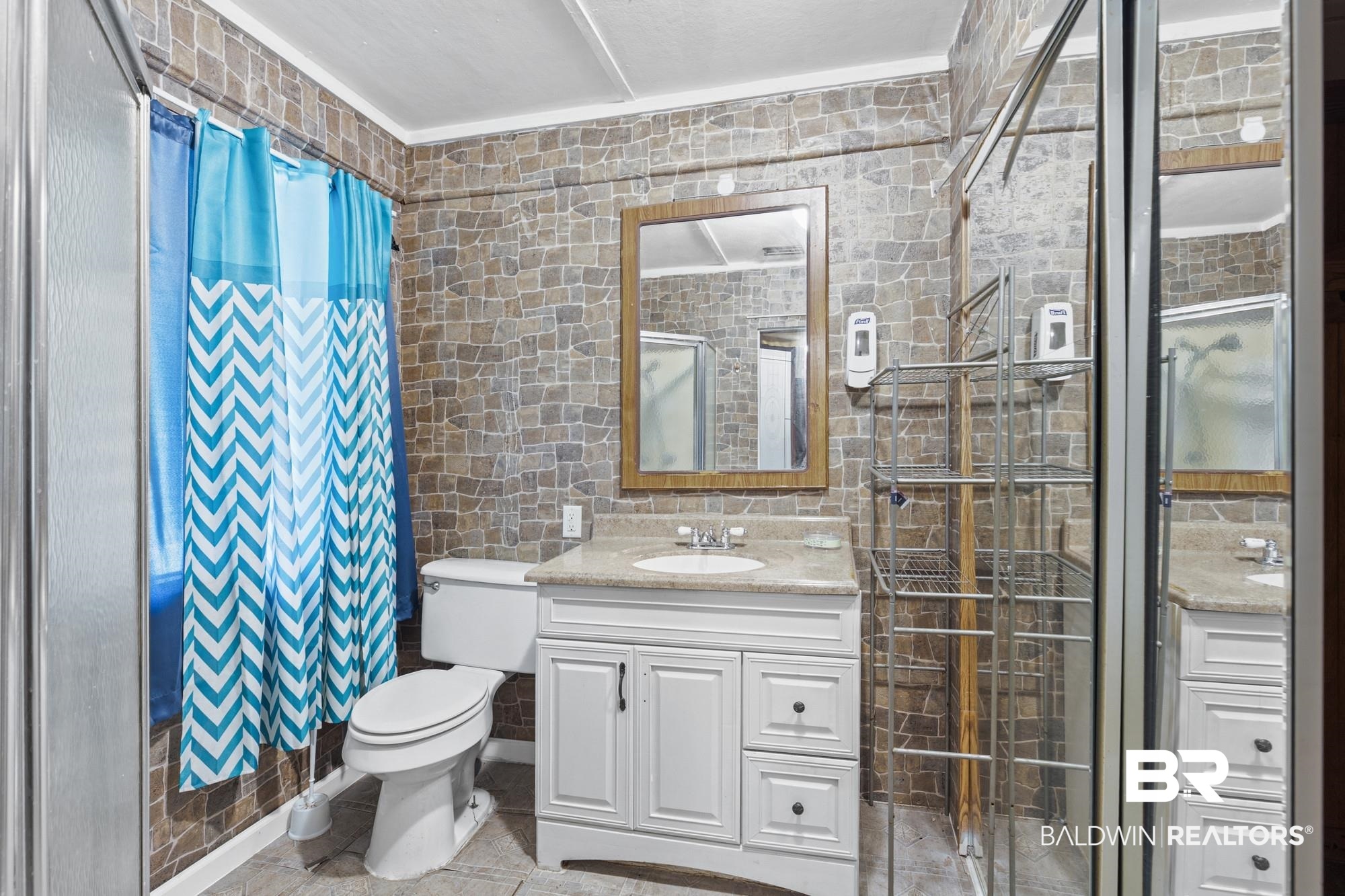 160 Glenn Avenue Mobile, AL 36606 - Photo 8 of 15 Full bathroom featuring stone-look wall tiling, a white vanity with a light-toned countertop, a framed mirror, and a glass-enclosed shower