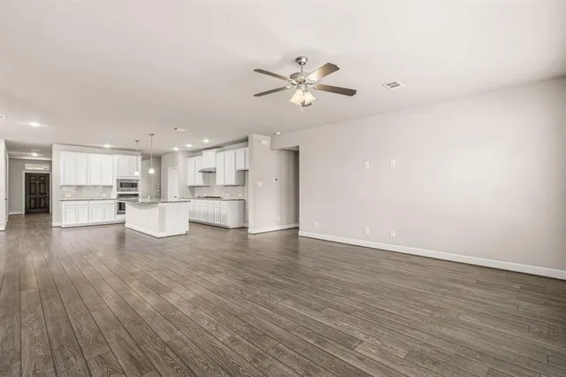 a view of an empty room with wooden floor and a kitchen