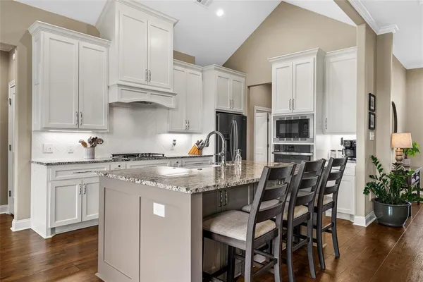 a kitchen with stainless steel appliances granite countertop a stove top oven a refrigerator a sink and white cabinets with wooden floor