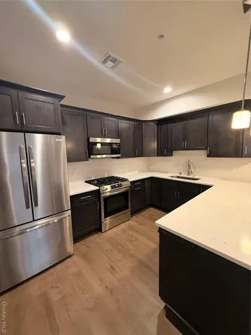 a kitchen with stainless steel appliances kitchen island a sink dishwasher a refrigerator and cabinets with wooden floor