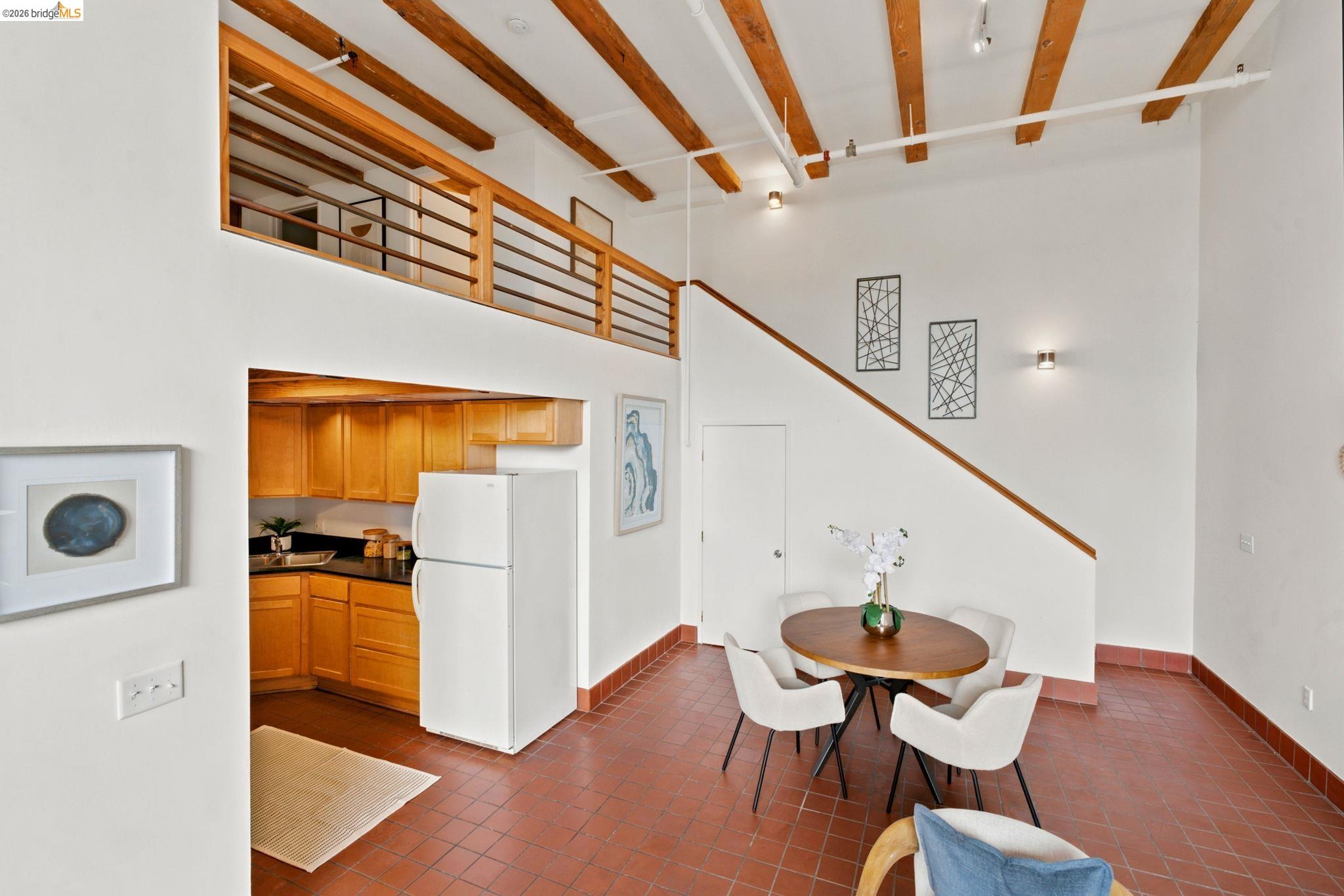 1920 Union Street, Unit 9 Oakland, CA 94607 - Photo 14 of 35 High-ceiling living area featuring exposed wood beams, a loft with wood and metal railings, and a built-in kitchen area with wood cabinetry and dark countertops