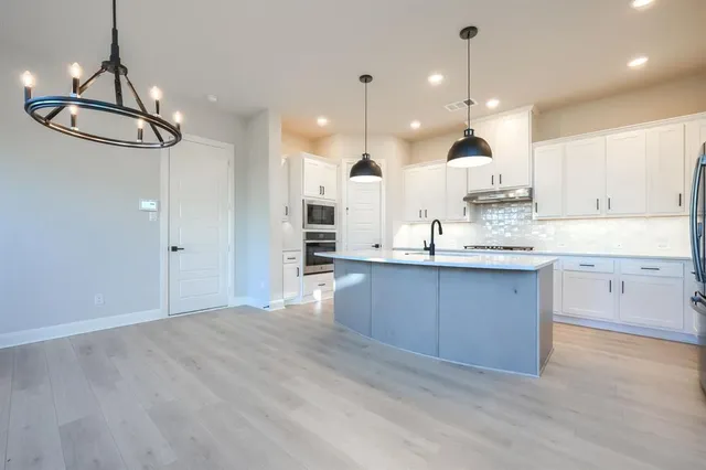 a large kitchen with kitchen island a stove a sink a center island and wooden floor