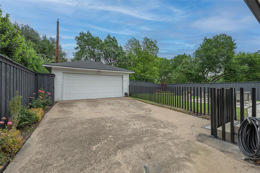 864 Peavy Road Dallas, TX 75218 - Photo 20 of 21 Detached garage with a white panel door, concrete driveway, and dark vertical slat fencing