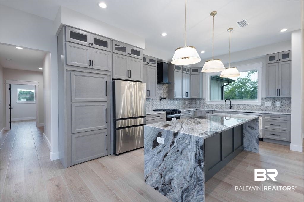 13066 Gopher Court Elberta, AL 36530 - Photo 5 of 38 Gourmet kitchen featuring a waterfall island with granite countertop, light gray cabinetry with black hardware, stainless steel appliances, recessed lighting, and wood-finish flooring.