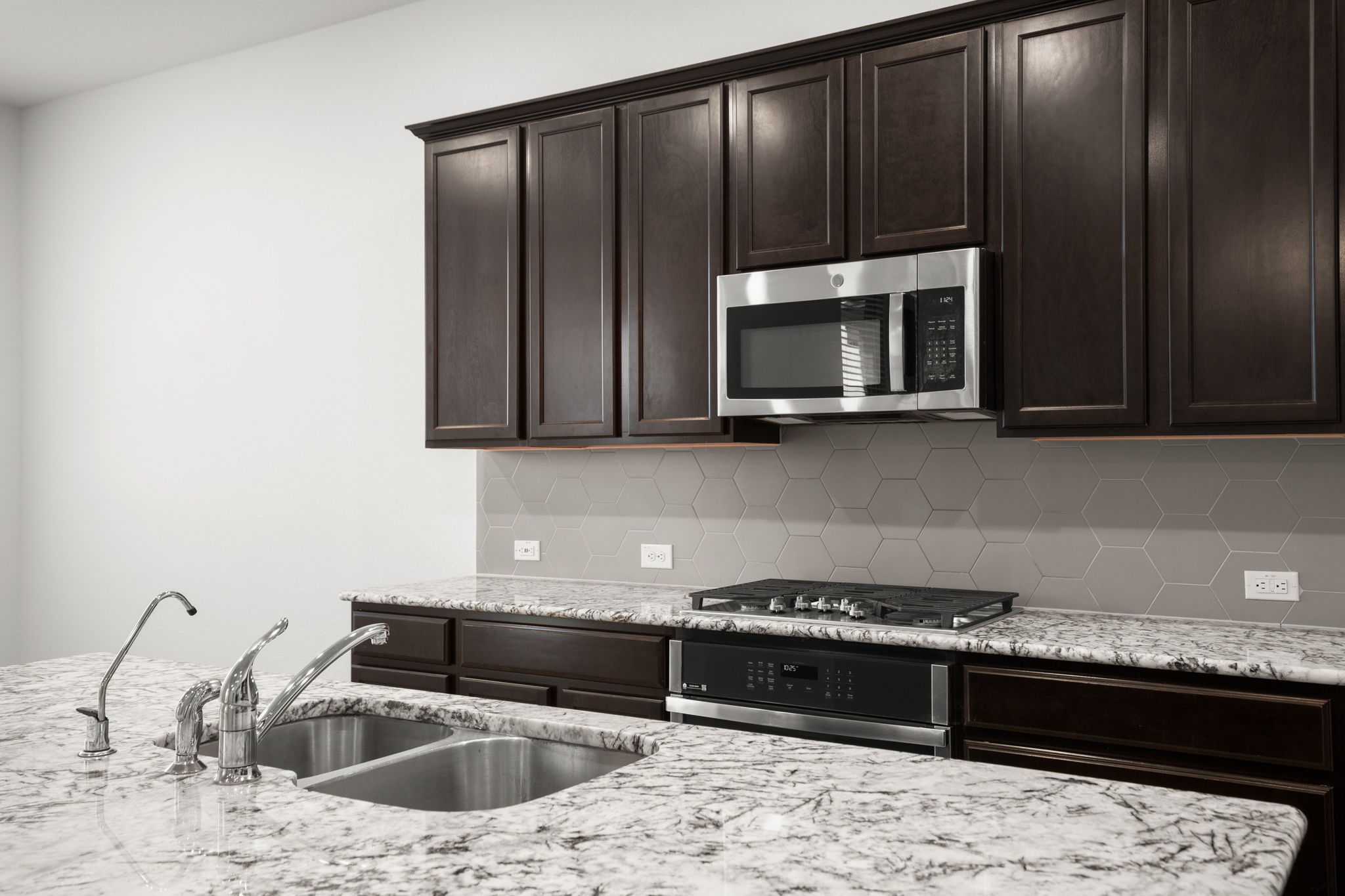 841 Spinnaker Loop Kyle, TX 78640 - Photo 18 of 40 Kitchen with dark brown cabinets, light stone counters, stainless steel appliances, and decorative backsplash