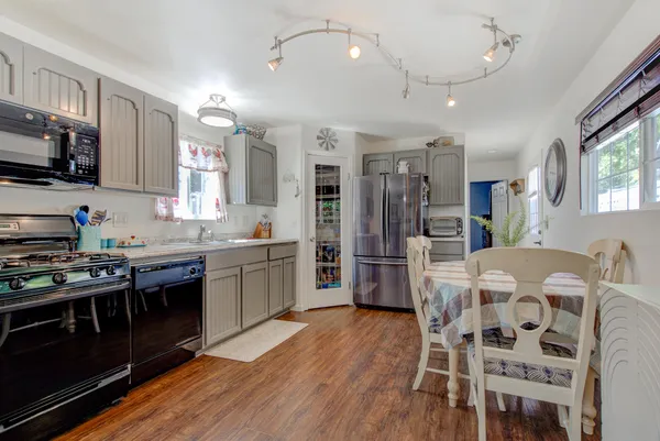 a kitchen with stainless steel appliances granite countertop a stove top oven a refrigerator a sink dishwasher a dining table and chairs with wooden floor