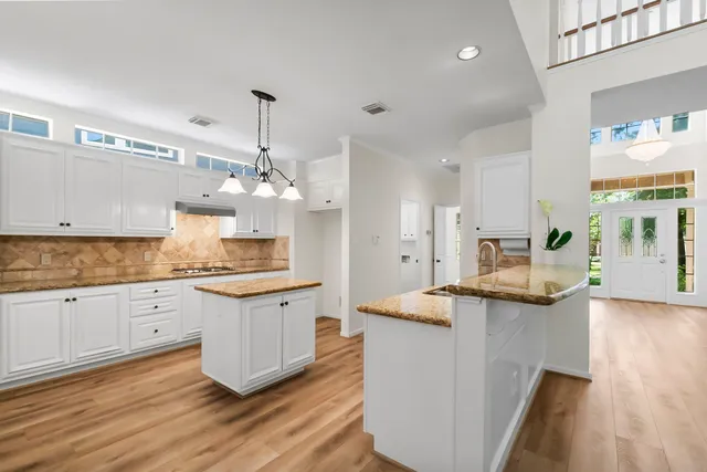 a kitchen with granite countertop a sink stove and white cabinets with wooden floor