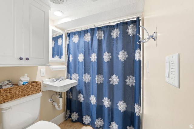 270 East 700 North Logan, UT 84321 - Photo 20 of 42 Compact bathroom featuring a wall-mounted sink, a toilet, an overhead storage cabinet, and a shower area with a curtain