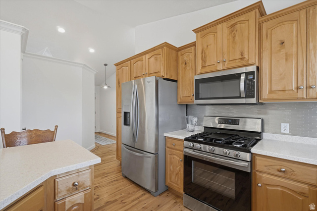 791 East Saddle Road Grantsville, UT 84029 - Photo 9 of 46 Modern kitchen featuring wood-finish flooring, light wood cabinetry, stainless steel appliances, light-toned countertops, and a textured metal backsplash