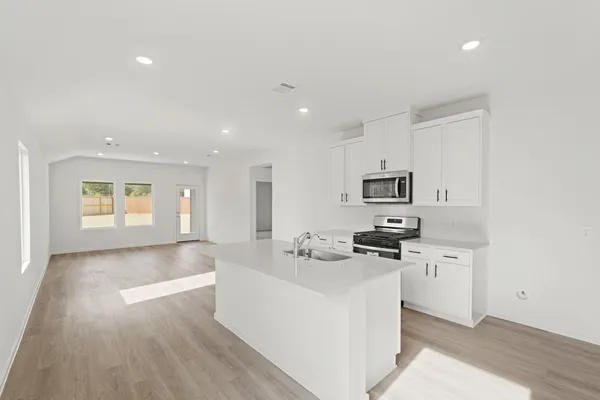 a large white kitchen with stainless steel appliances granite countertop a stove a sink a refrigerator and white cabinets with wooden floor