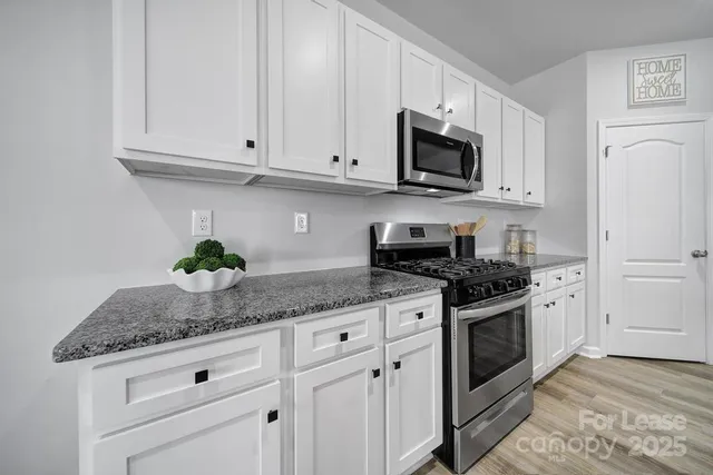 a kitchen with granite countertop white cabinets stainless steel appliances and a counter space