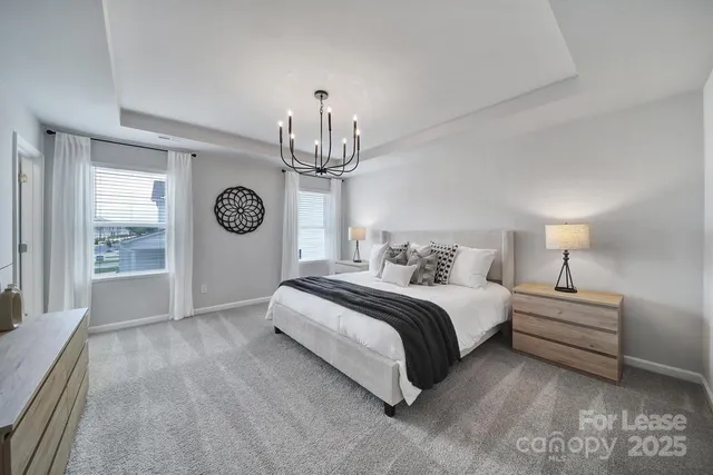 a spacious bedroom with a bed a chandelier and windows