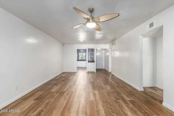 a view of an empty room with wooden floor and a ceiling fan
