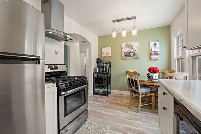 a kitchen with stainless steel appliances granite countertop a refrigerator a stove and a dining table with wooden floor