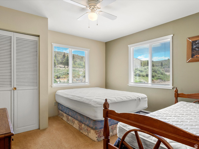 85 B Street, Unit 22 St. Charles, ID 83272 - Photo 22 of 35 Bright bedroom featuring two windows with horizontal blinds, a ceiling fan with integrated lighting, and louvered closet doors
