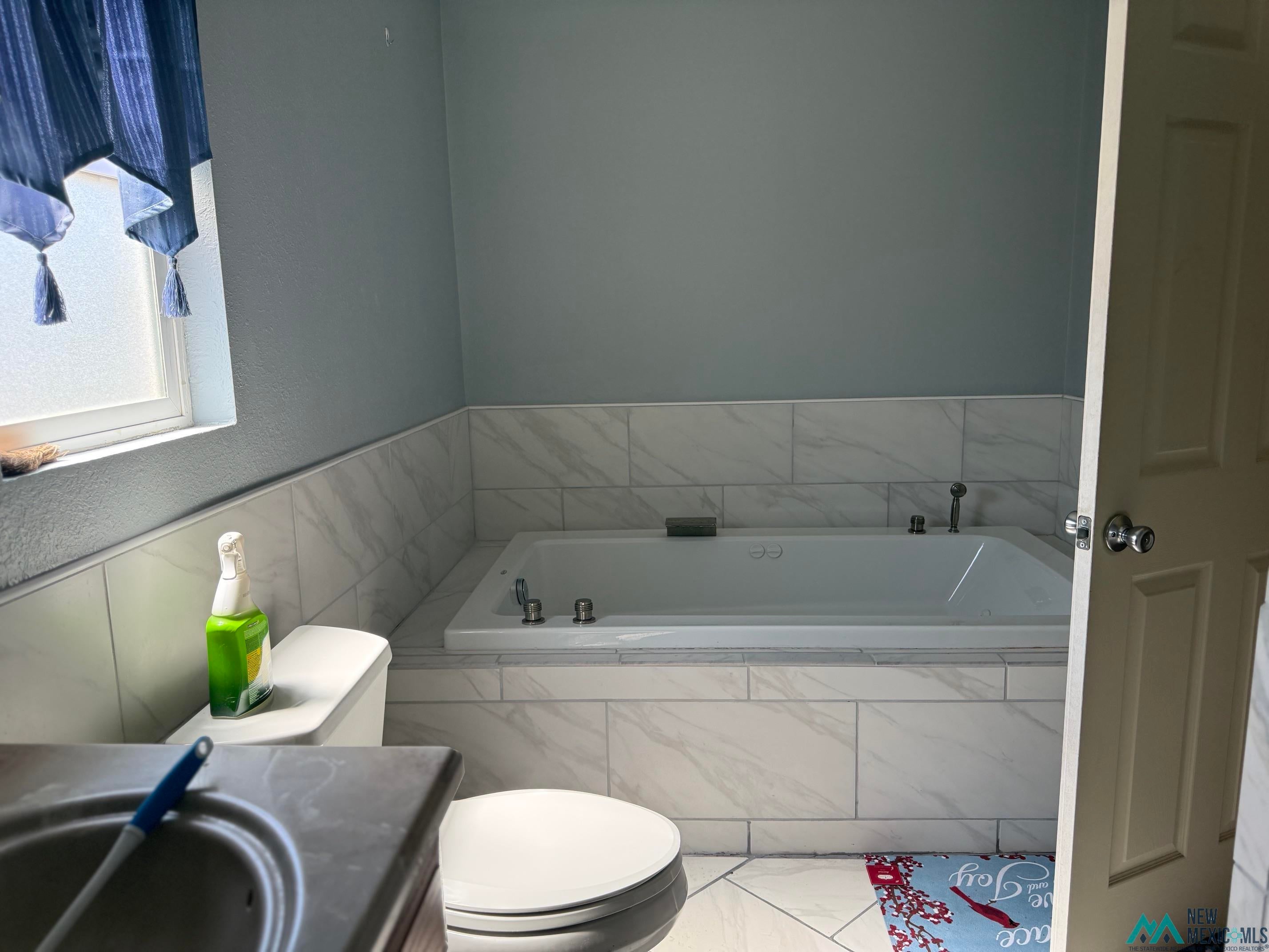 104 Shawnee Road Logan, NM 88426 - Photo 25 of 36 Built-in soaking tub with deck-mounted fixtures, surrounded by large format white tile with grey veining