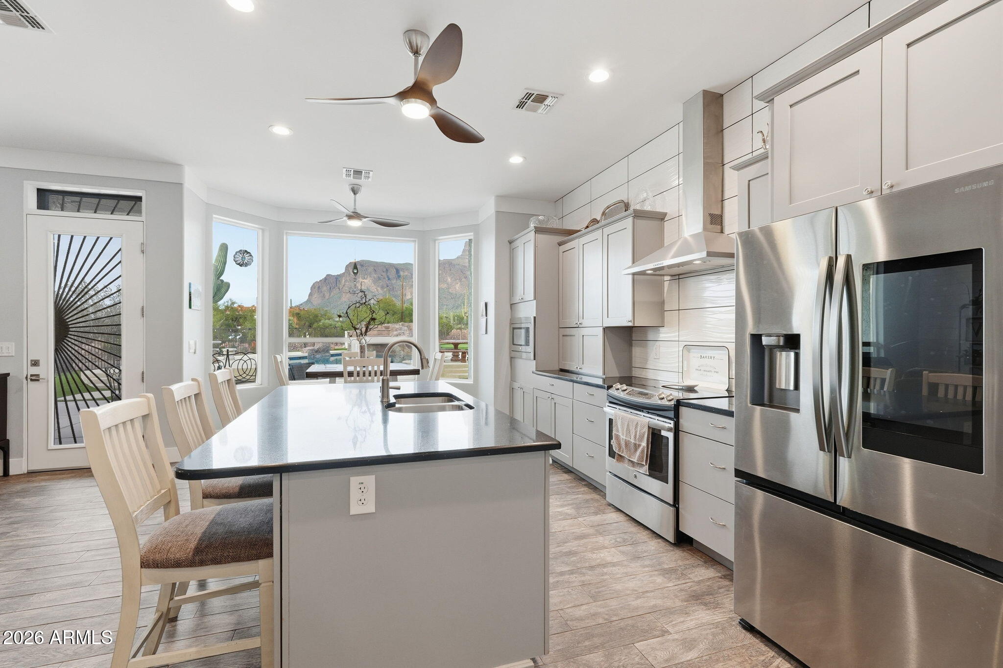 1067 South Trigger Court Apache Junction, AZ 85119 - Photo 20 of 60 a large kitchen with stainless steel appliances kitchen island granite countertop a refrigerator a stove a sink a dining table and chairs with wooden floor