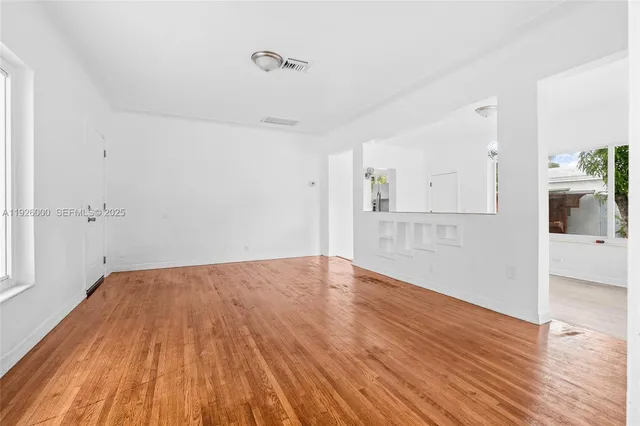 a view of empty room with wooden floor and kitchen