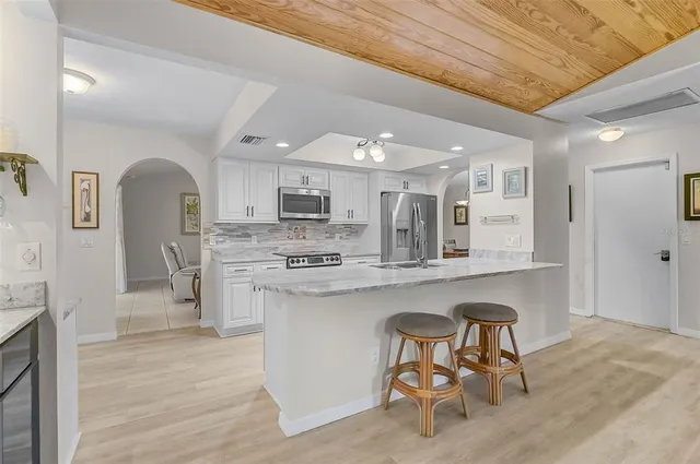 a kitchen with stainless steel appliances a microwave a stove a sink dishwasher and white cabinets with wooden floor