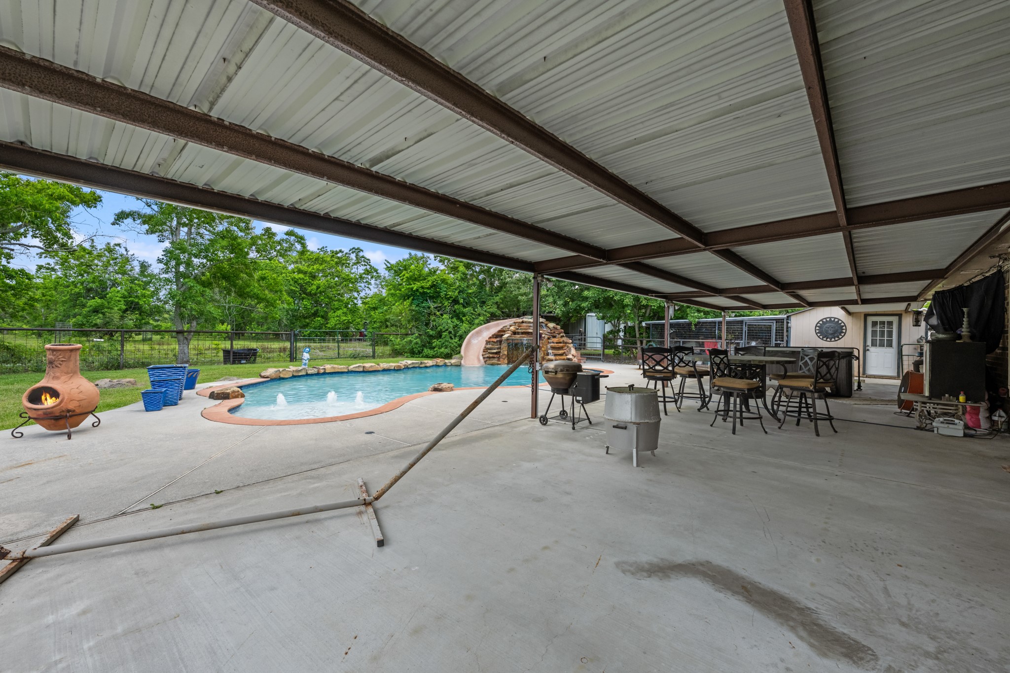 15602 Fir Road Santa Fe, TX 77517 - Photo 28 of 42 Resort-style backyard featuring a sparkling pool with rock waterfall slide, expansive covered patio, and multiple seating areas designed for outdoor entertaining. The spacious setup offers the perfect blend of relaxation, recreation, and year-round enjoyment.
