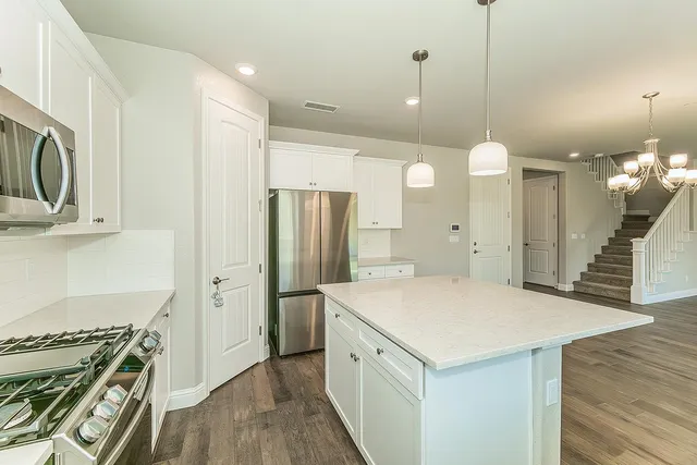 a kitchen with stainless steel appliances a stove a refrigerator a sink and white cabinets with wooden floor