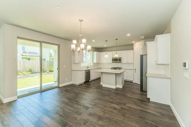 a open kitchen with a refrigerator a sink dishwasher a stove and a dining table with wooden floor