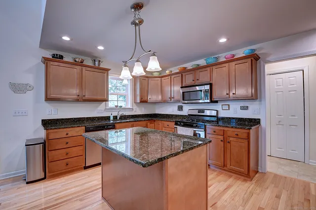 a kitchen with stainless steel appliances granite countertop wooden cabinets and a wooden floor