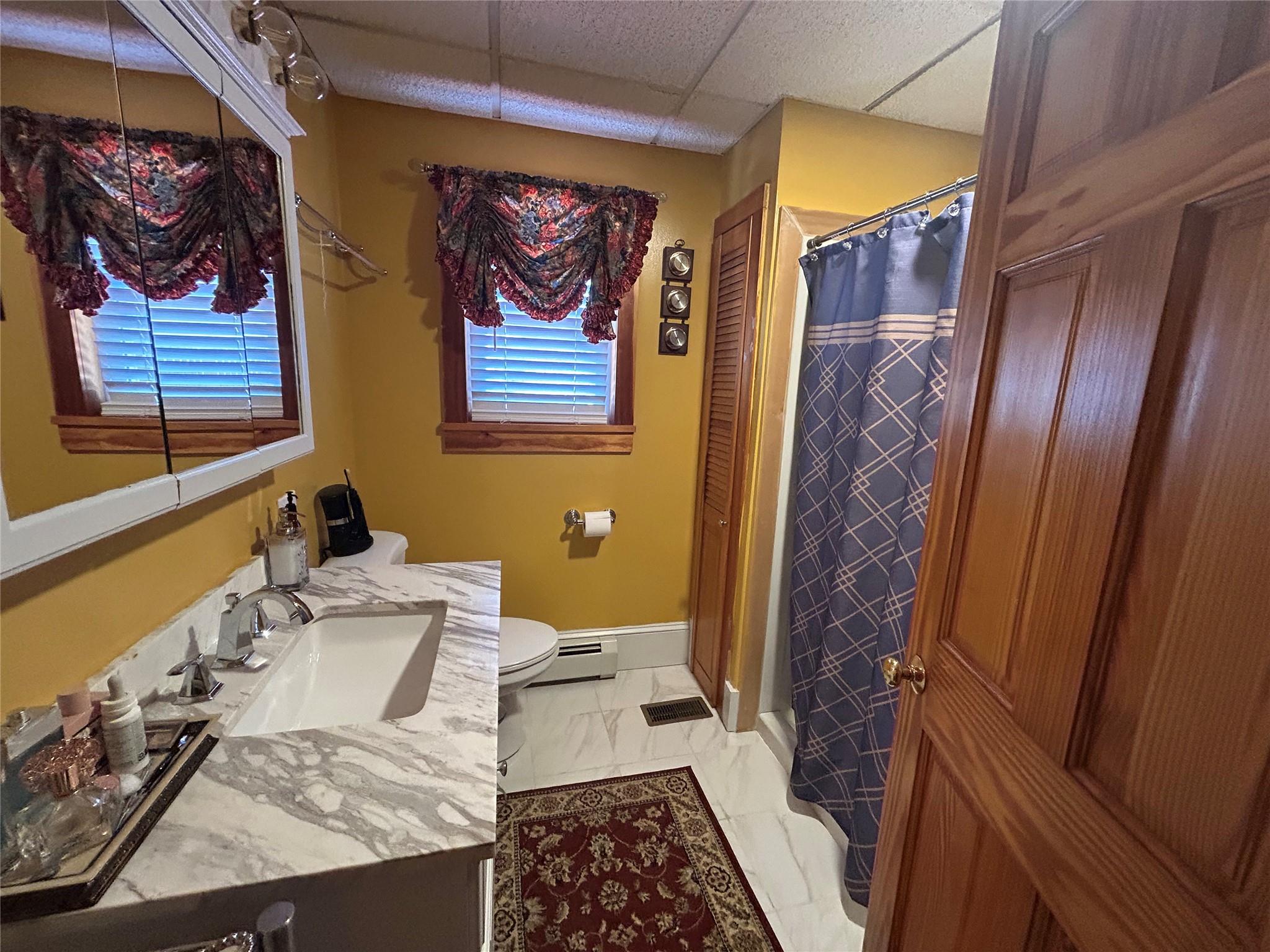 199 Washington Street Poughkeepsie, NY 12601 - Photo 15 of 32 Bathroom featuring a drop ceiling, toilet, a baseboard heating unit, vanity, and marble finish floor