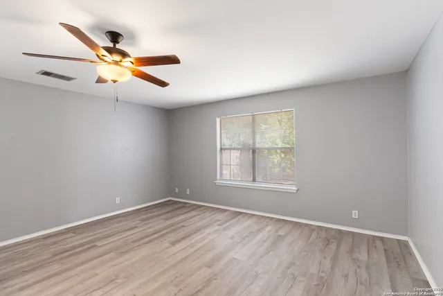 an empty room with wooden floor fan and windows