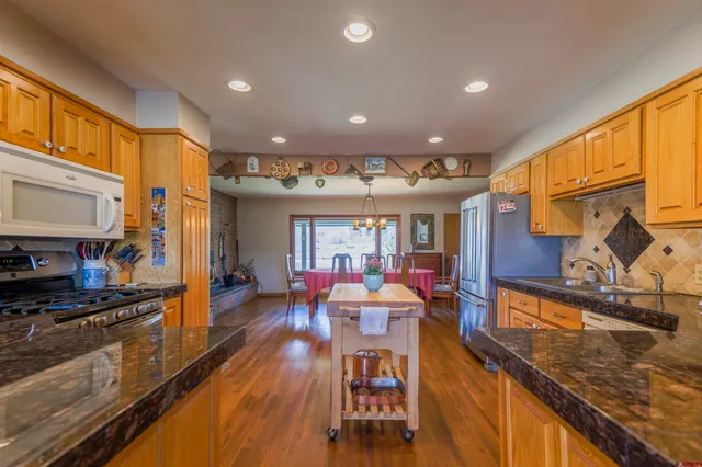 a kitchen with stainless steel appliances granite countertop a refrigerator a stove a sink dishwasher and a dining table with wooden floor