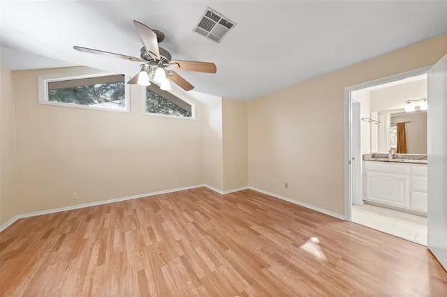 an empty room with wooden floor chandelier fan and windows