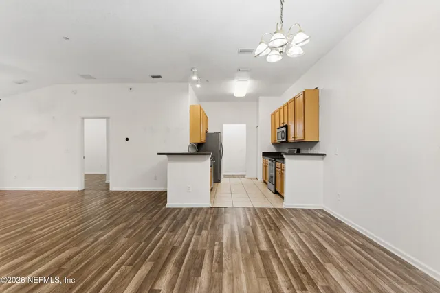 a view of kitchen and empty room with wooden floor