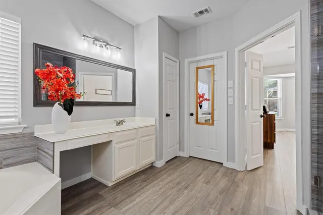 a view of a hallway to room with wooden floor mirror and a window