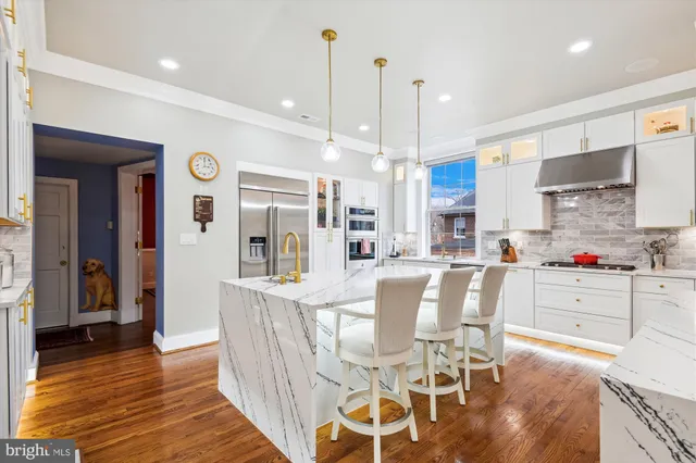 a kitchen with stainless steel appliances kitchen island granite countertop a refrigerator a stove and white cabinets with wooden floor