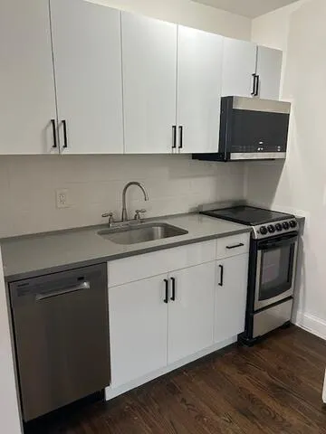 a kitchen with stainless steel appliances granite countertop a sink a stove and white cabinets with wooden floor