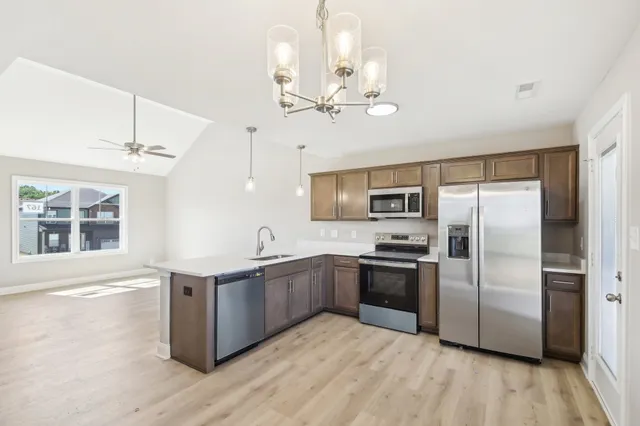 a kitchen with stainless steel appliances granite countertop a refrigerator a sink dishwasher a stove and a dining table with wooden floor