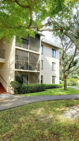 a view of a white house next to a yard with big trees
