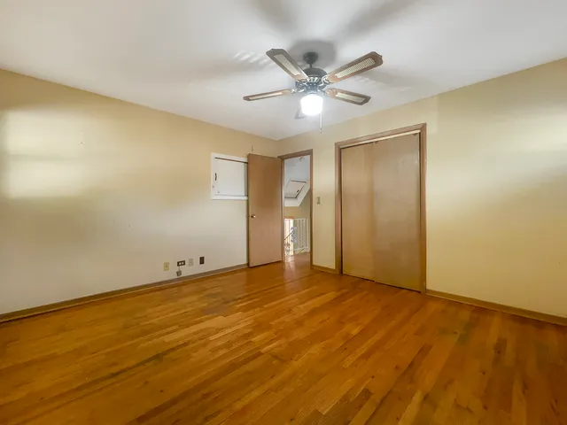 a view of an empty room with wooden floor and a ceiling fan