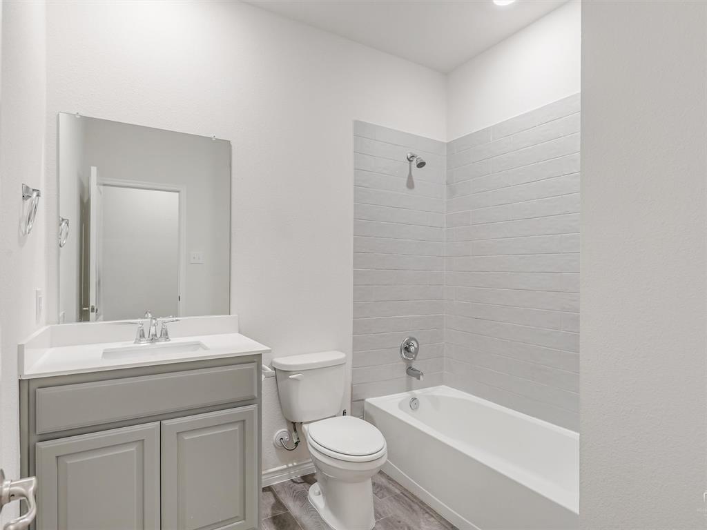 3024 Meredith Lane Forney, TX 75126 - Photo 18 of 29 Full bathroom featuring a single vanity with gray cabinetry and a white countertop, a toilet, and a combined shower and bathtub with light gray horizontal tile surround