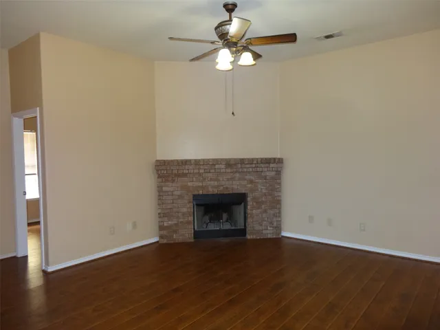 an empty room with wooden floor a chandelier fan and a fireplace